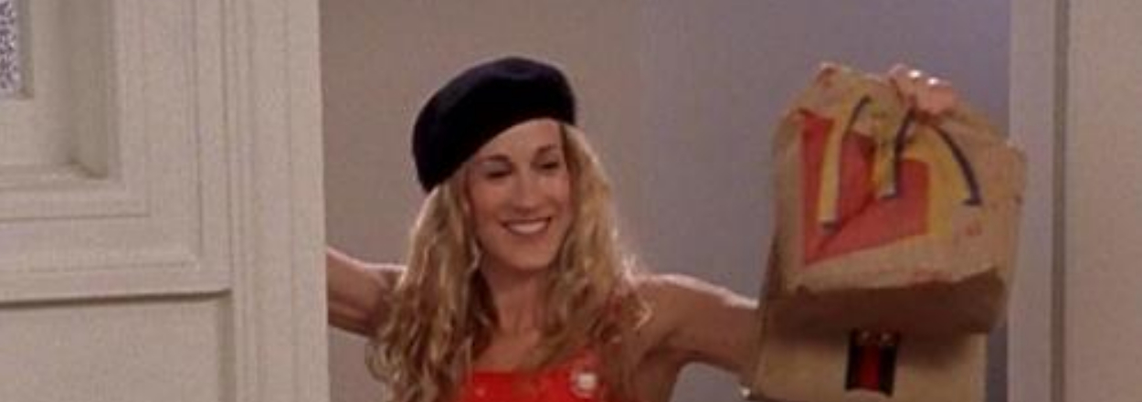 Phoebe Buffay from Friends smiles holding a paper bag, styled in a red polka dot dress and black beret