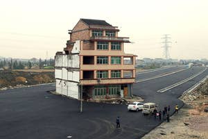 Isolated house stands in the middle of a newly built road with a group of people nearby discussing