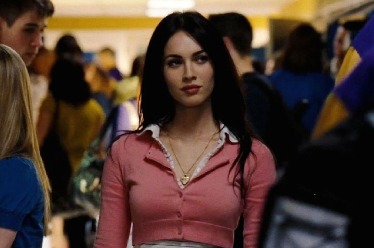 Megan Fox wearing a pink top and white necklace in a crowded hallway