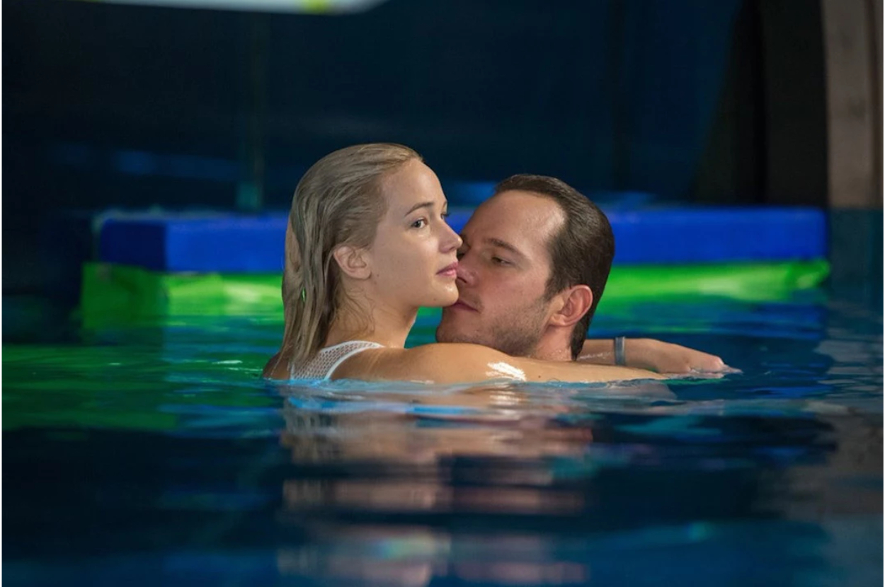 Two characters from a film share an intimate moment in a pool, man behind hugging the woman
