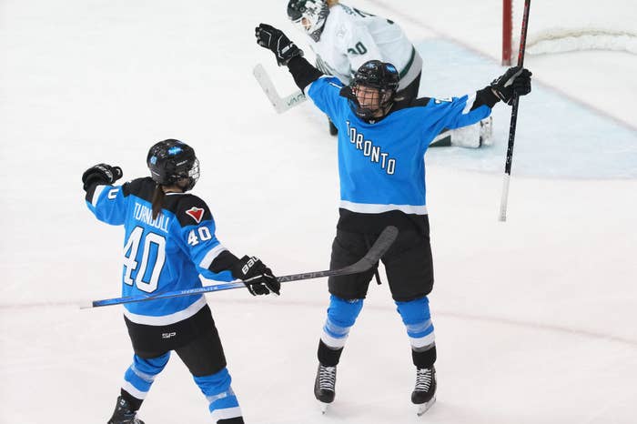 Two hockey players in Toronto uniforms celebrating a goal on the ice with the goalie in the background