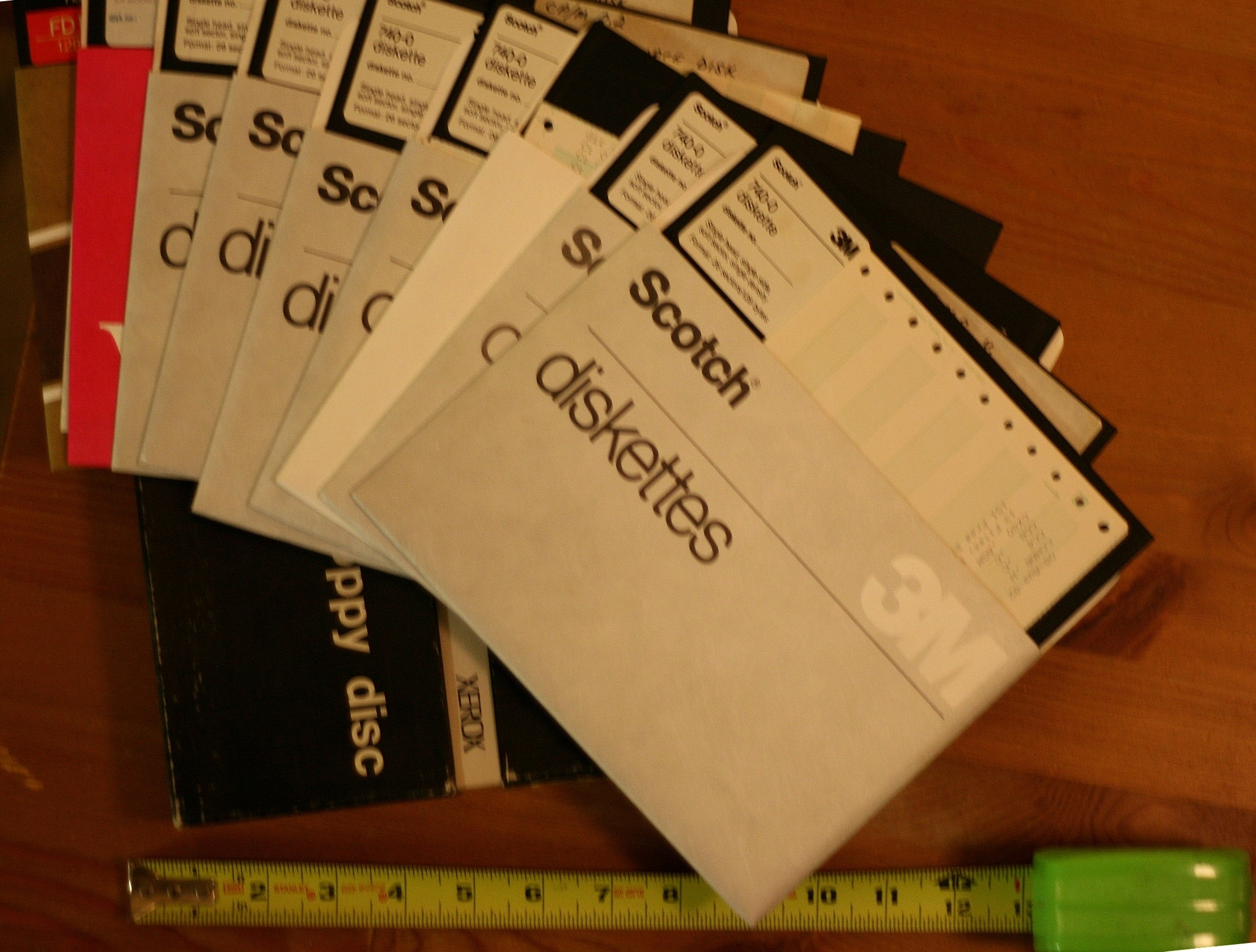 A collection of vintage labeled floppy disks spread out, next to a ruler for scale
