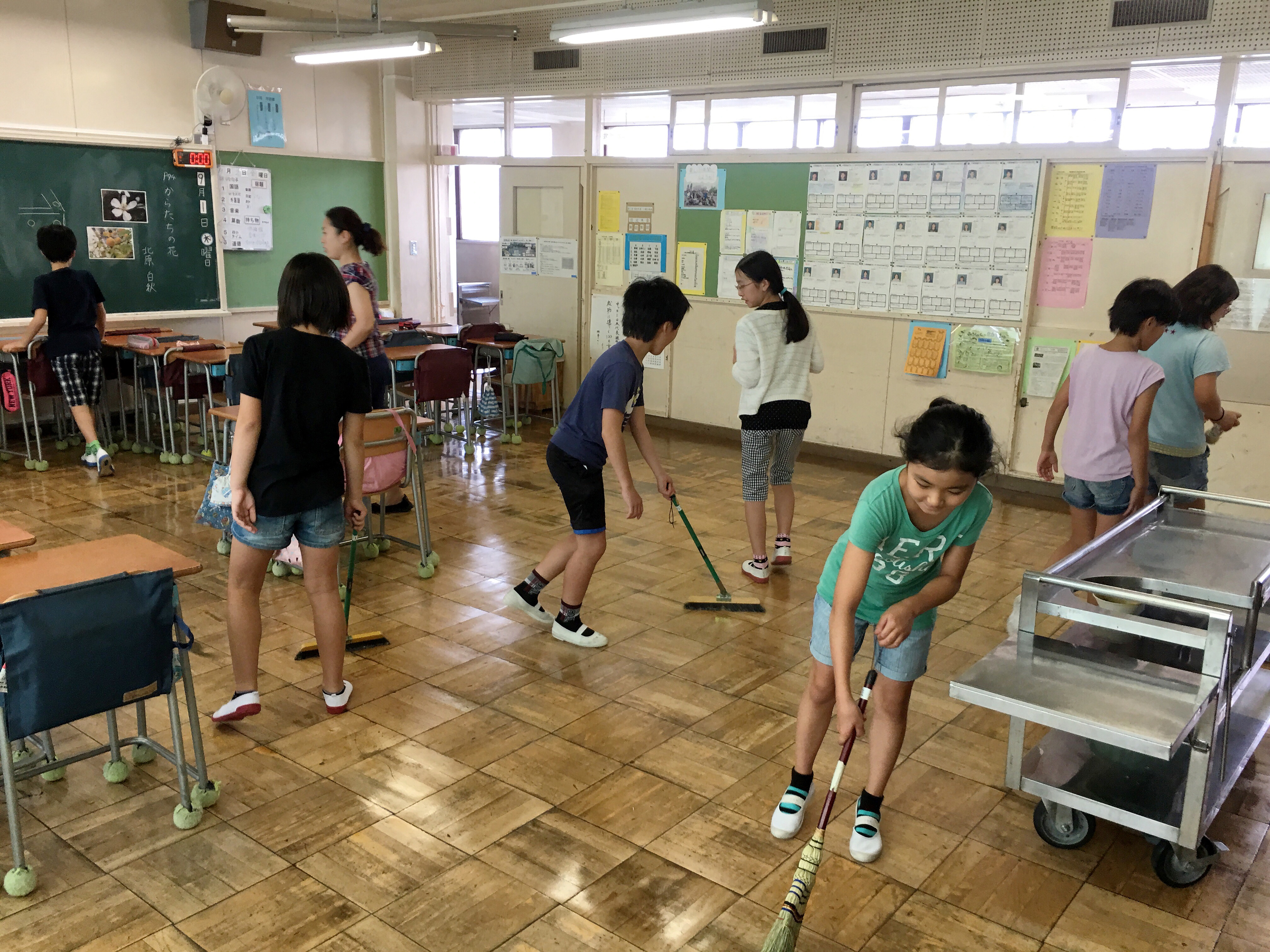 Students participate in cleaning a classroom with brooms and cloths