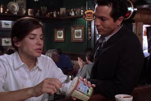Two actors in a scene at a diner, woman passing condiment to man in suit