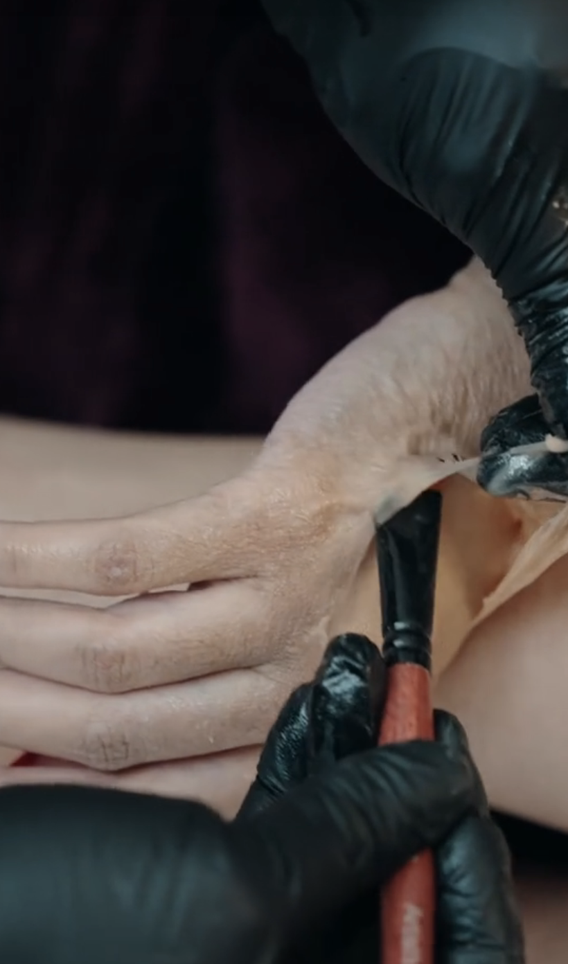 Someone applying prosthetics to Cardi&#x27;s hand