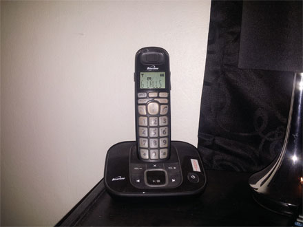 Cordless landline phone on a charging base next to a lamp on a desk