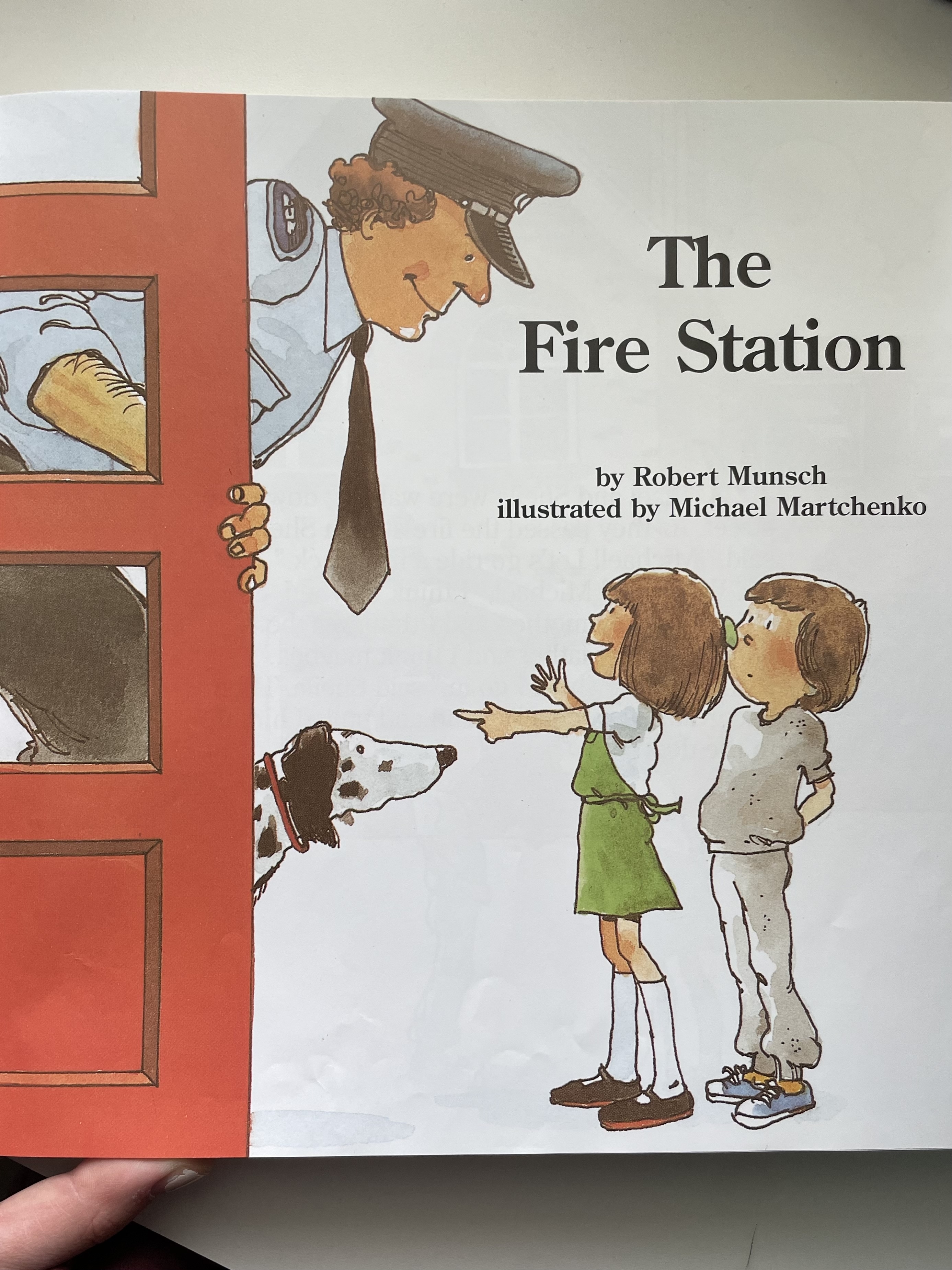 Cover of &quot;The Fire Station&quot; book showing an illustration of a firefighter, a Dalmatian dog, and two children