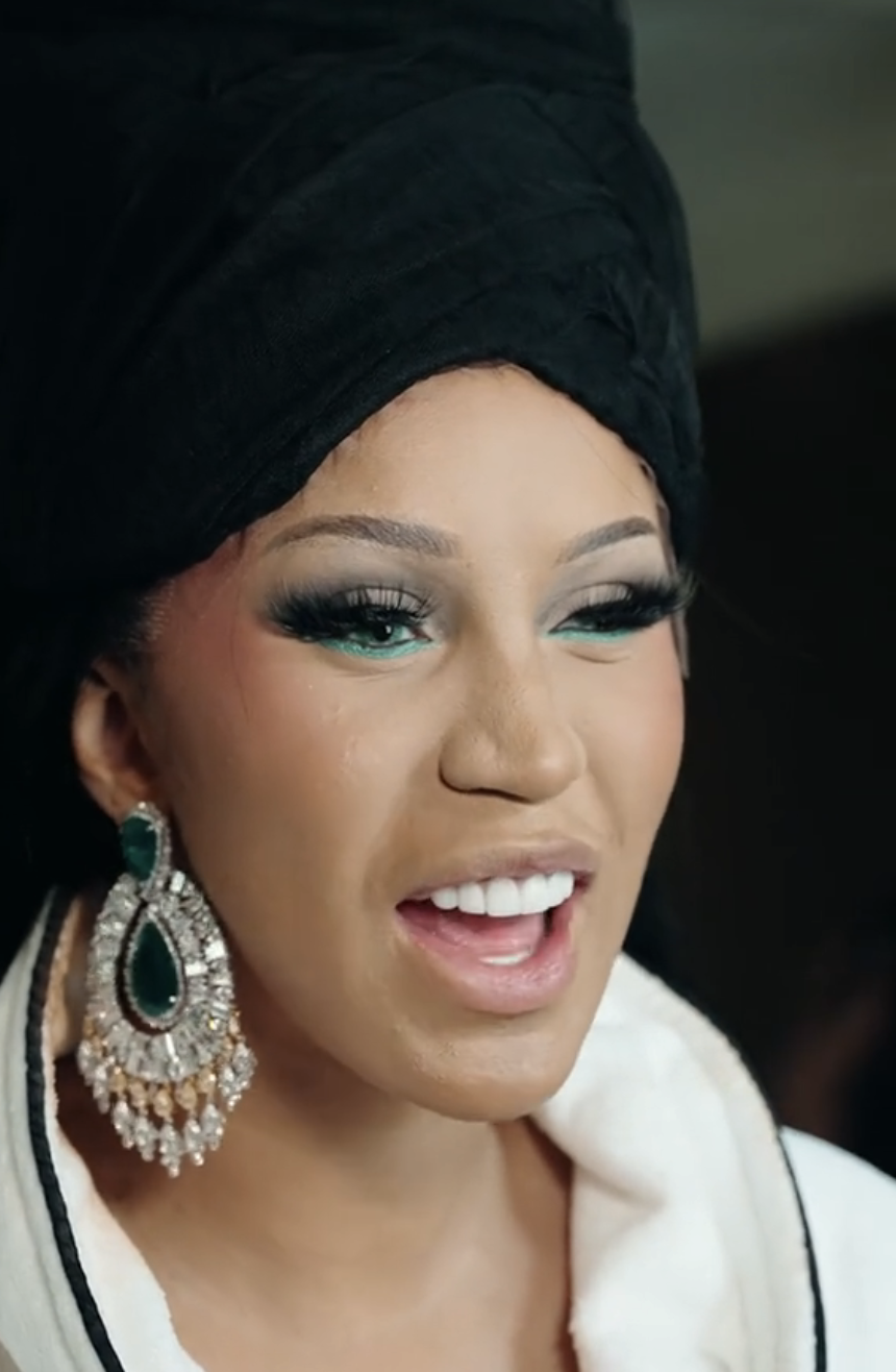 Close-up of Cardi B smiling, wearing a large head wrap and ornate earrings