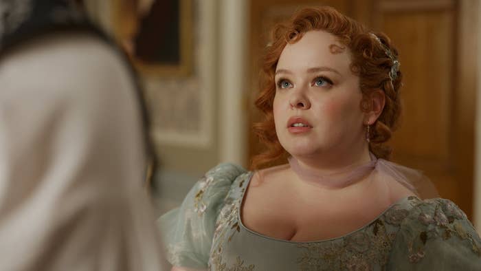 Bridgerton character Penelope Featherington, in a Regency-era dress, looking pensive during a scene