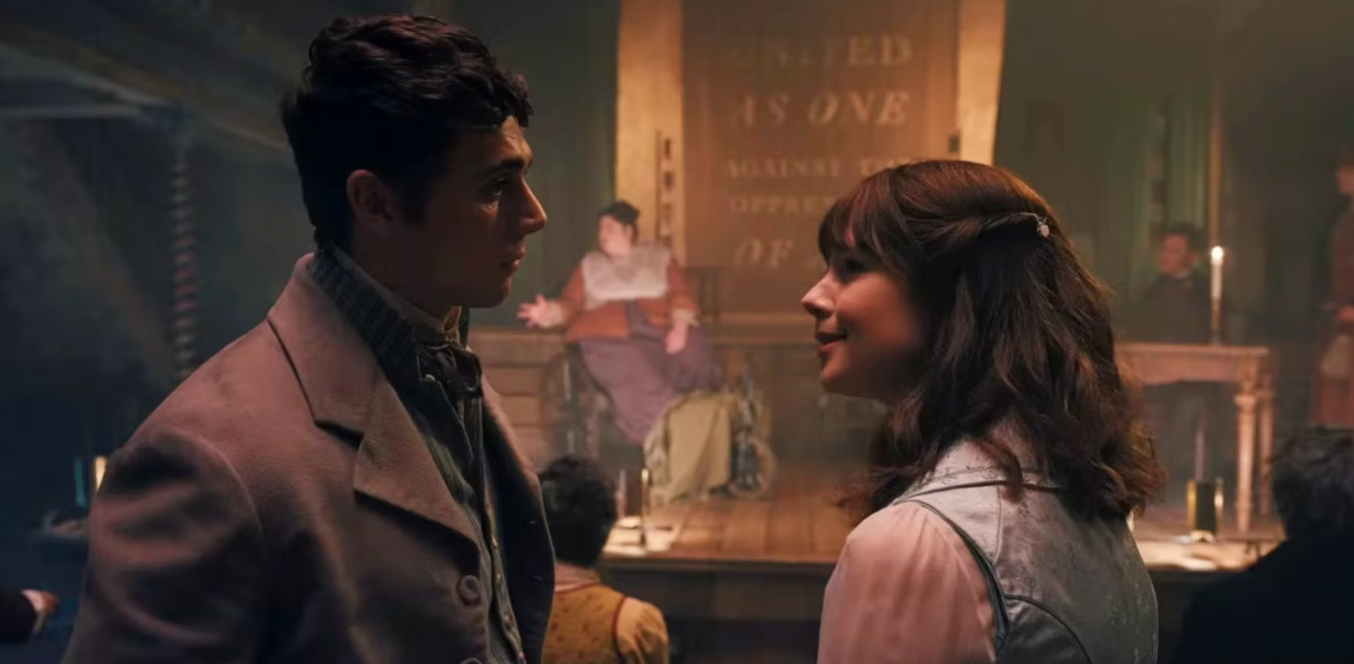 Two actors in period costume facing each other with a romantic gaze in a dimly-lit vintage setting