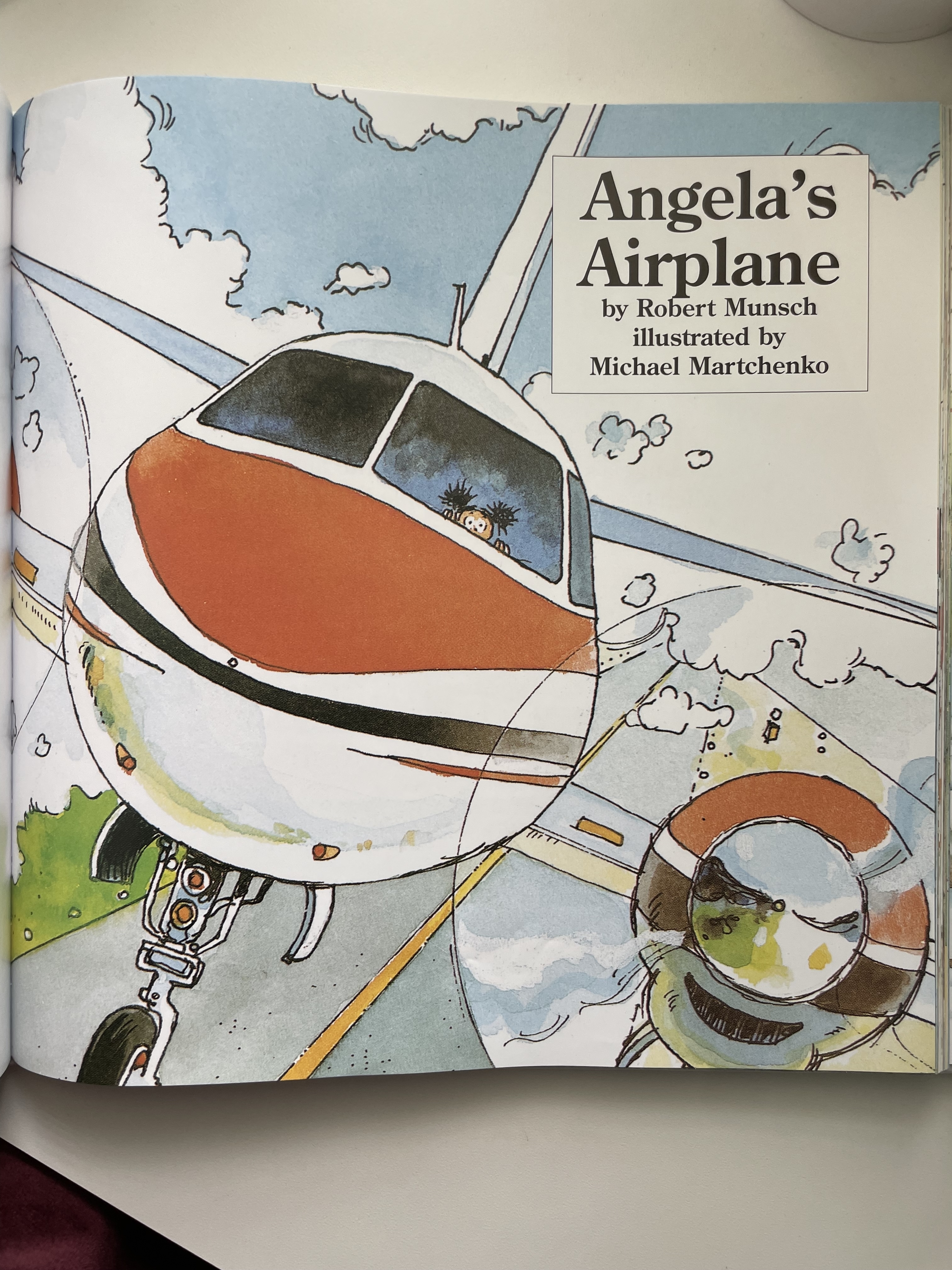 Book page showing title &quot;Angela&#x27;s Airplane&quot; by Robert Munsch, illustrated by Michael Martchenko, with artwork of a plane
