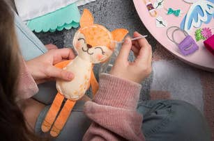 person sewing together a fox-shaped plush toy