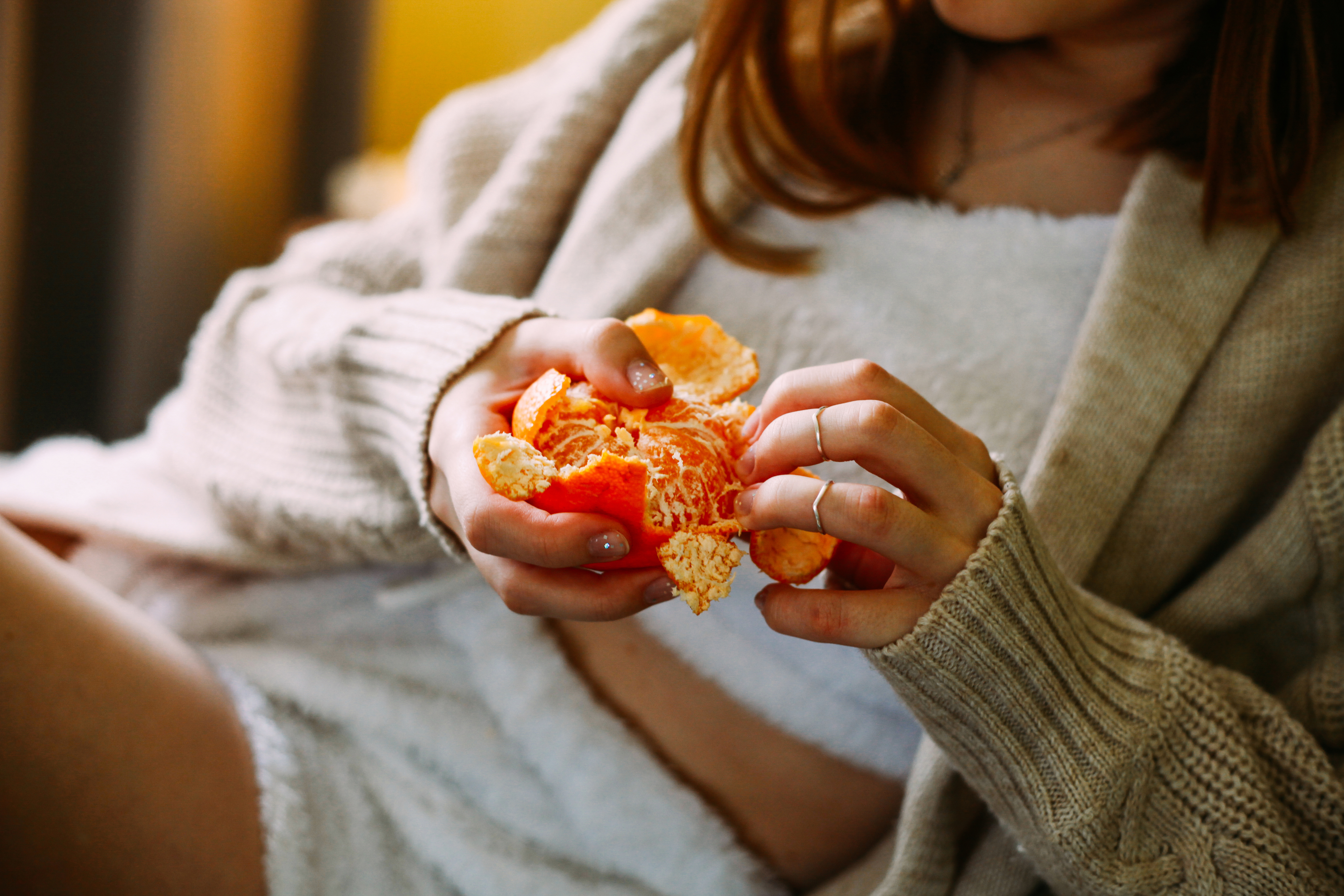 Person peeling an orange with both hands, wearing a cozy beige cardigan
