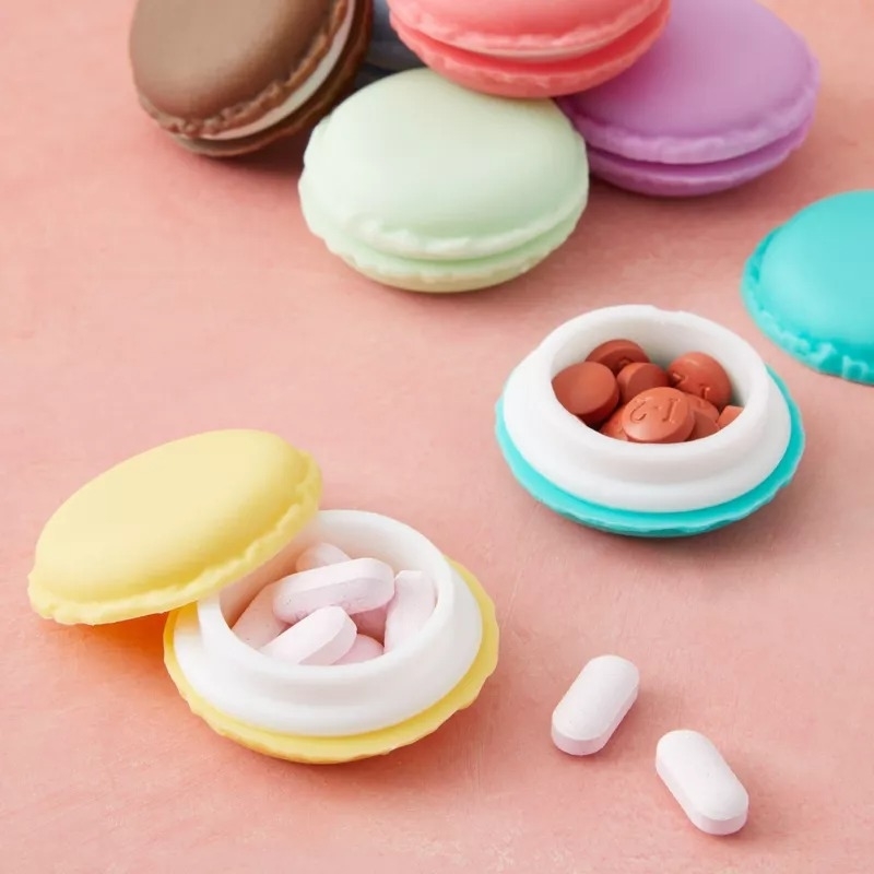 Colorful macaron-shaped pill organizers on a table, two closed and two open with pills inside
