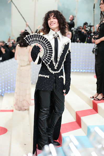 Person in a unique black and white sequined outfit with a fan-shaped accessory on a staircase