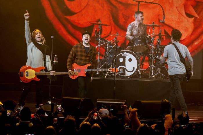 Fall Out Boy members performing on stage with instruments in front of an audience