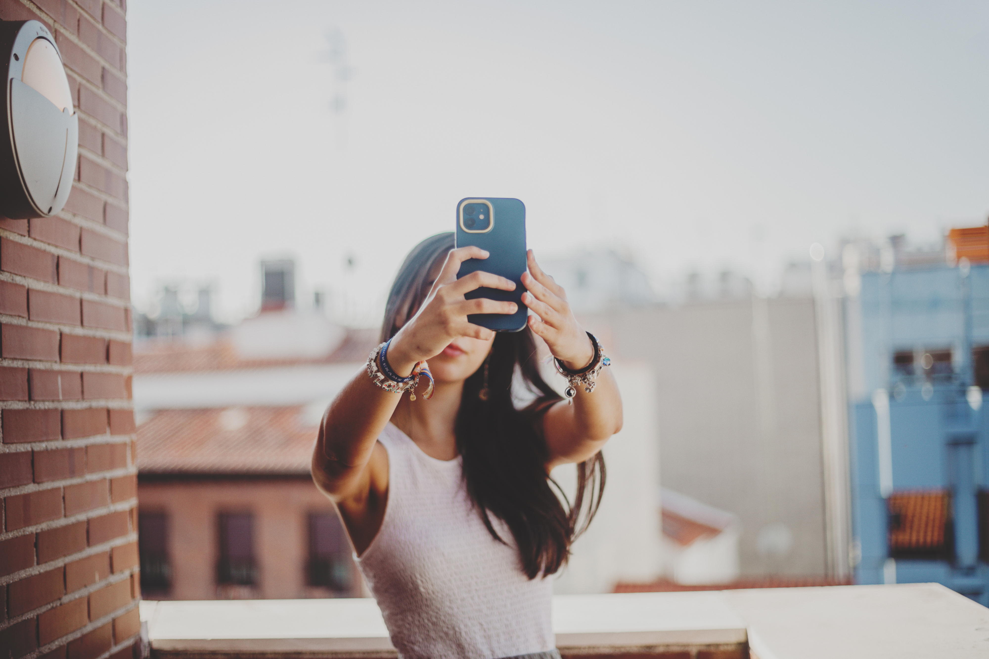 Woman taking a selfie on a balcony with smartphone, facing away from camera