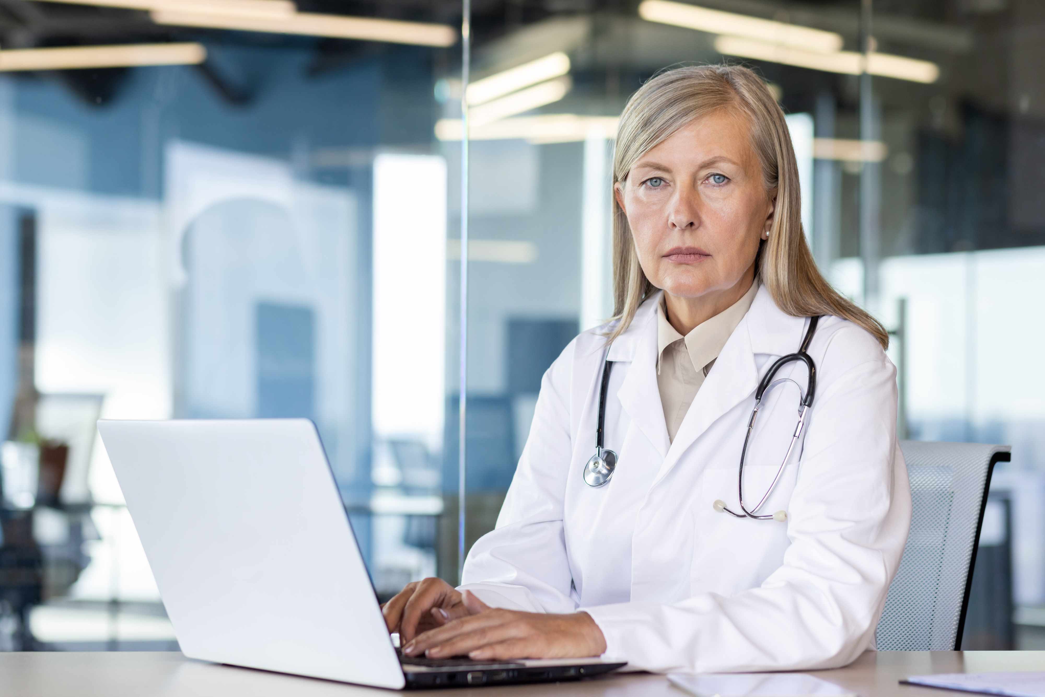 A focused female doctor with a stethoscope typing on a laptop in an office setting