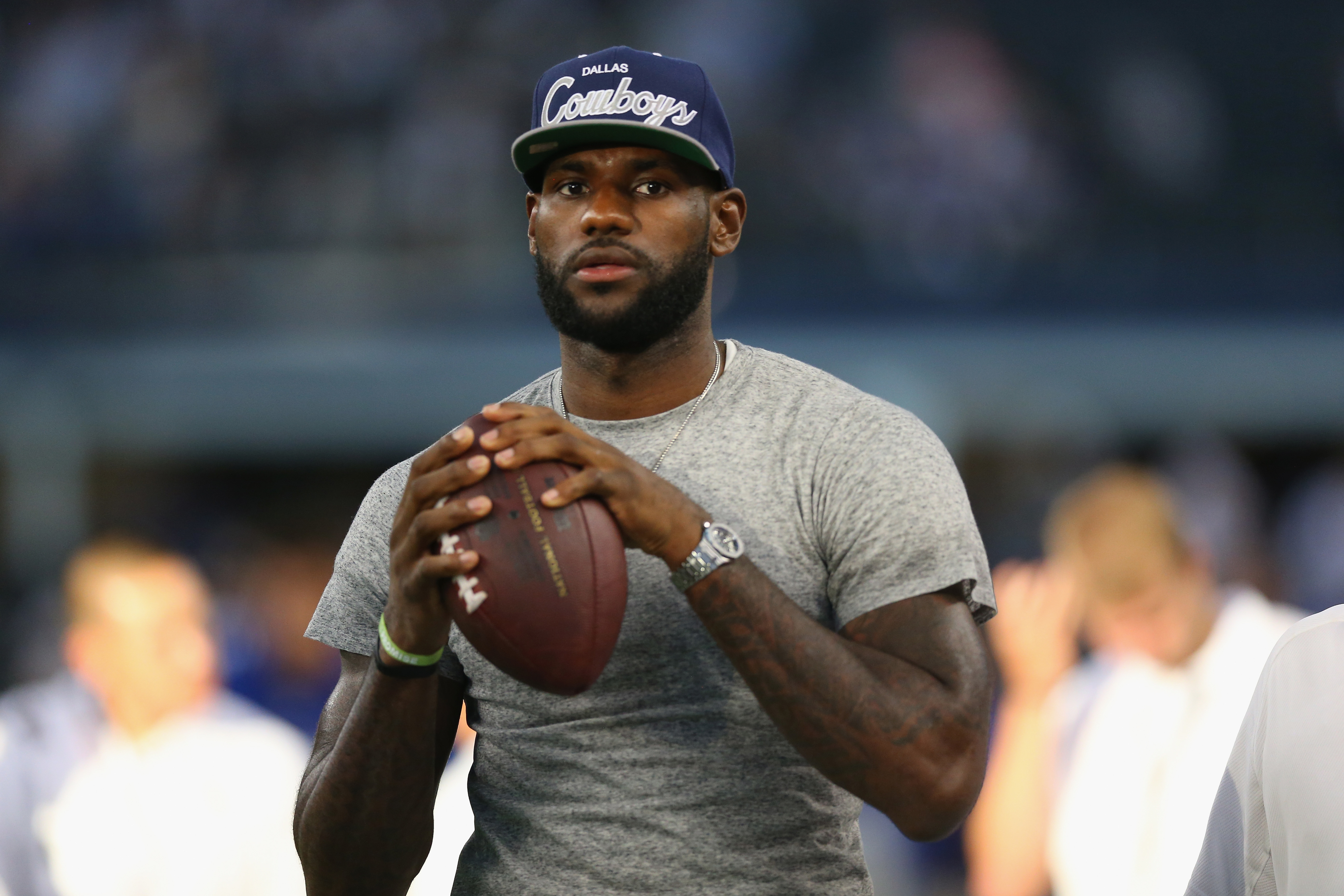 A man wearing a Dallas Cowboys cap prepares to throw an American football