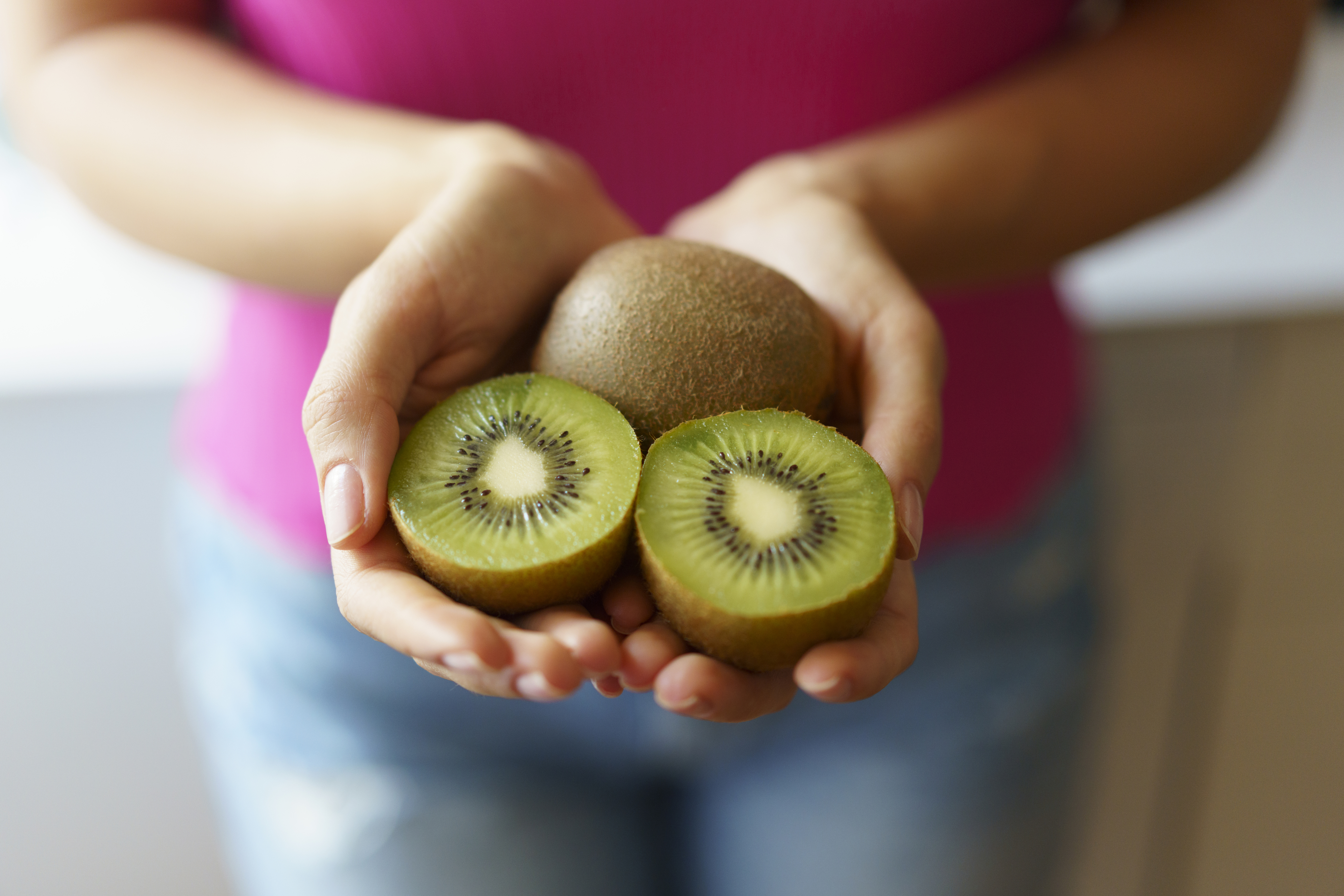 Person holding a sliced kiwi and a whole kiwi, promoting healthy eating habits
