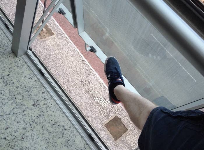 Person&#x27;s leg extended stepping onto a balcony with a clear floor, overlooking lower floors