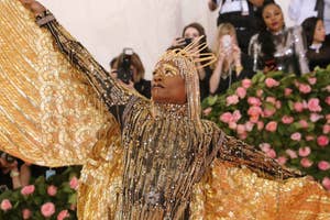 Person in a beaded headpiece and gold, glittering outfit with wide sleeves, posing with arms outstretched