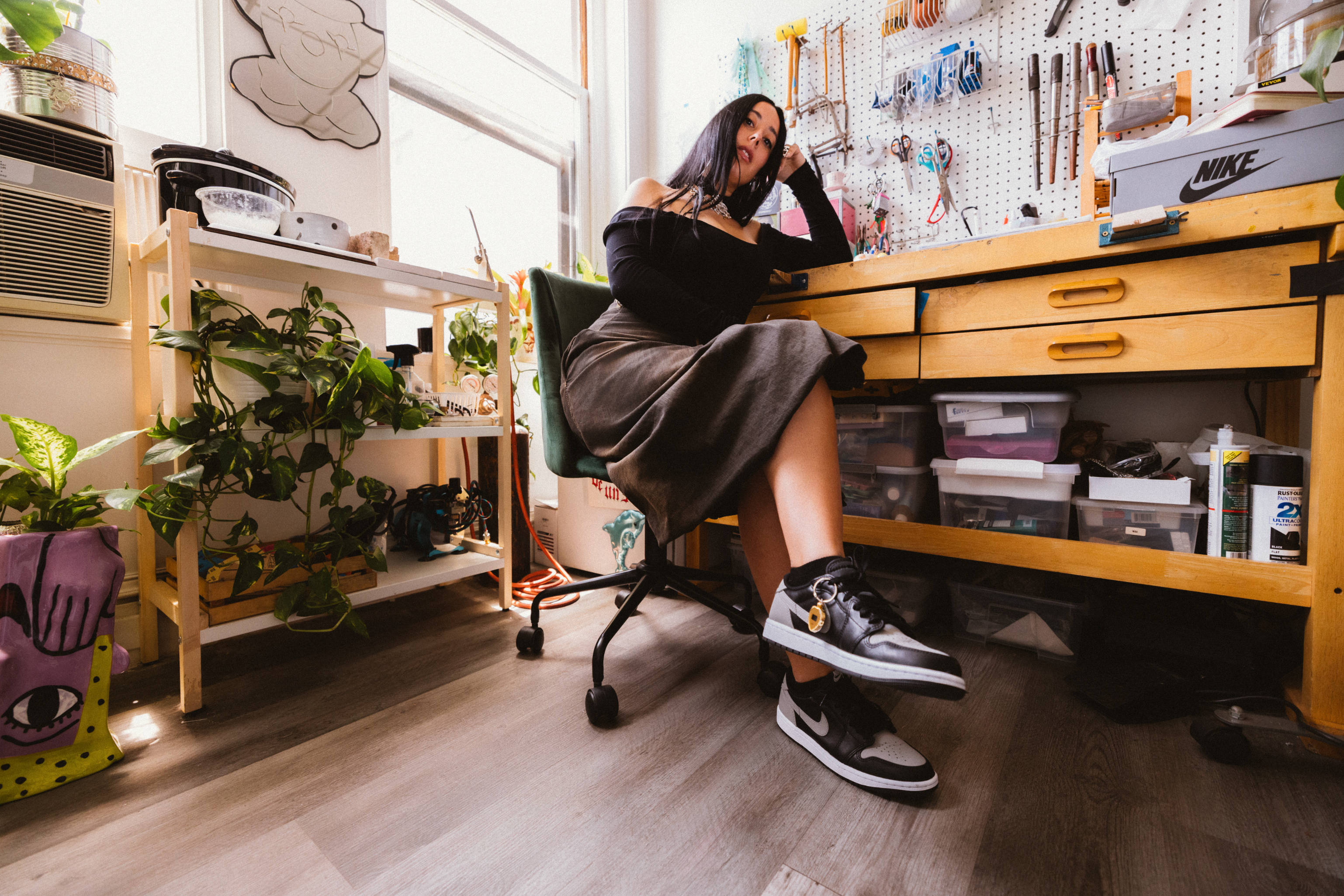 Person sitting by a desk with Nike sneakers on display, surrounded by art supplies and plants