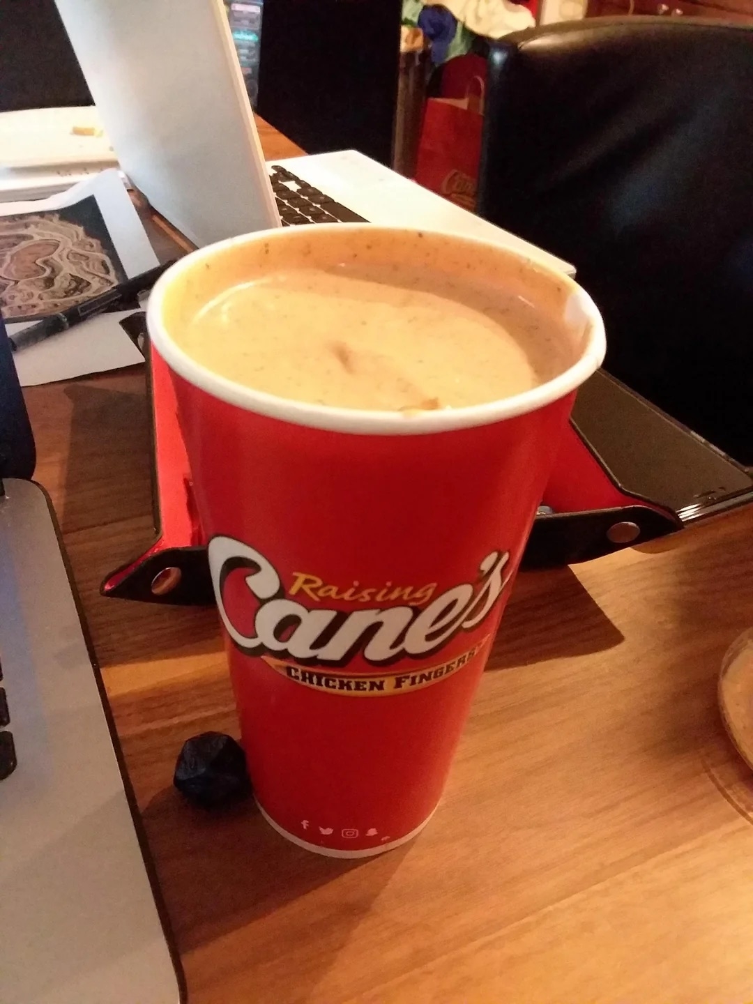 Raising Cane&#x27;s cup filled with sauce on a desk with a laptop in the background