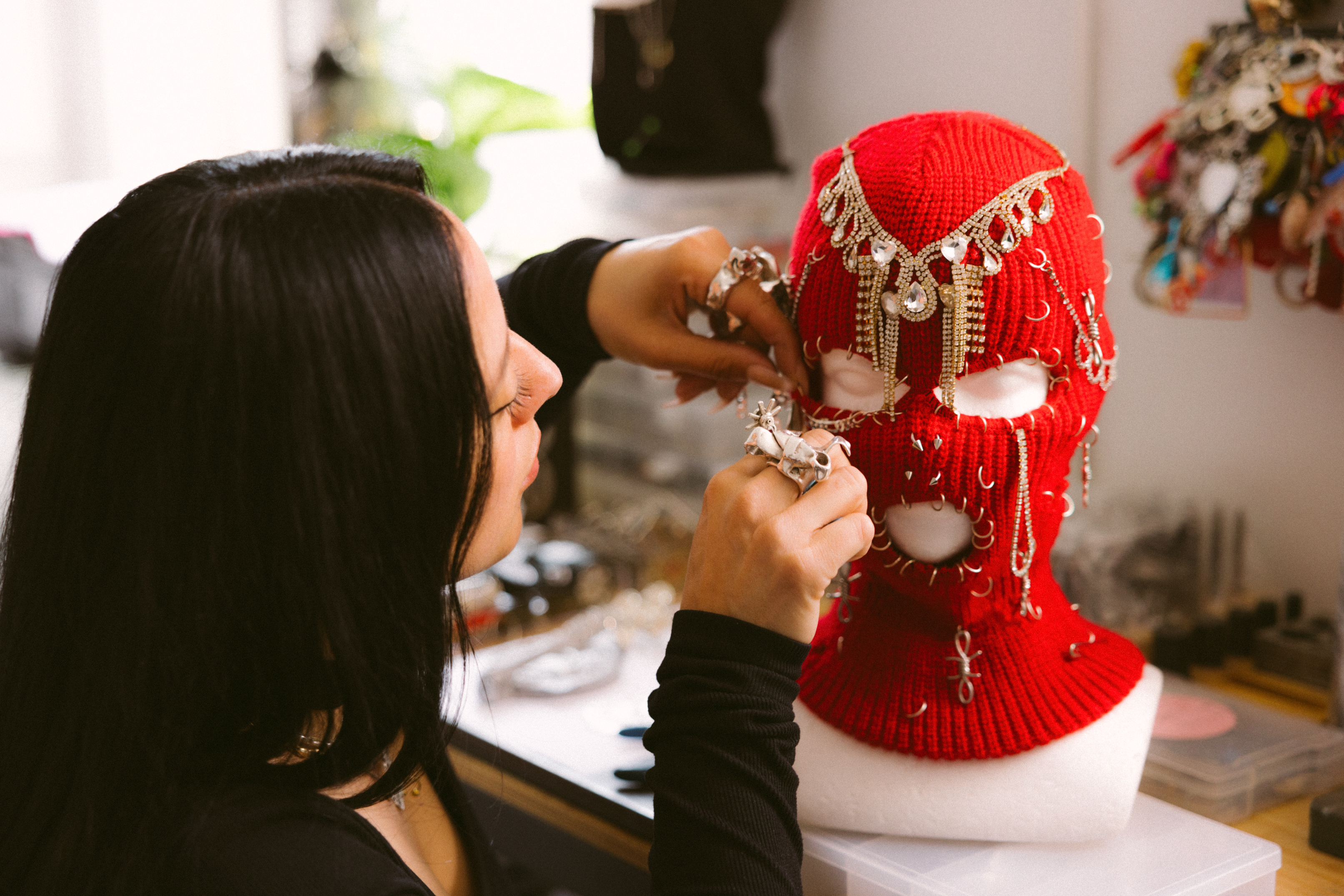A person customizing a red knit sneaker with embellishments and jewelry