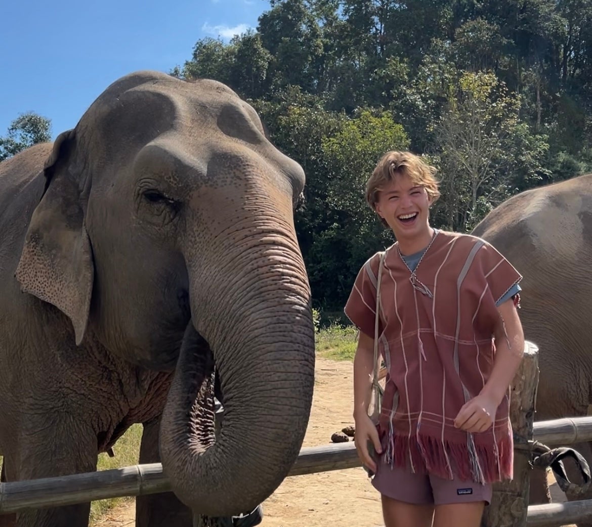 Person in striped outfit smiling next to an elephant