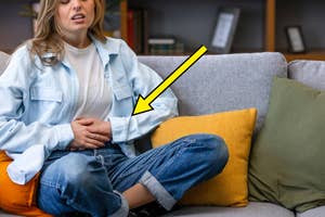 Woman on couch appearing discomforted, hand on abdomen, yellow arrow pointing to stomach