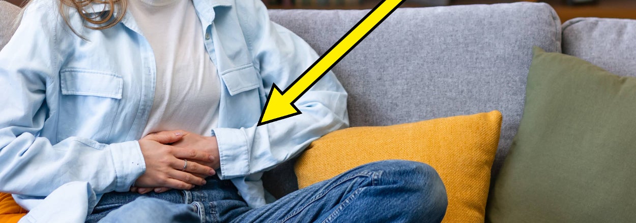 Person on couch appears uncomfortable with a possible stomach issue, denoted by an arrow