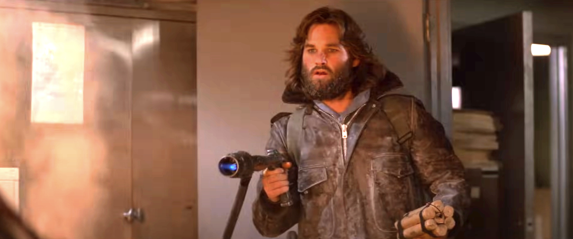 Jason Momoa as a rugged character holding a weapon, in a tense scene from a movie