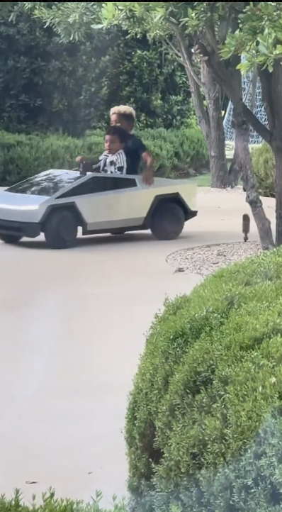 Two people riding in a futuristic-looking electric car through a garden pathway