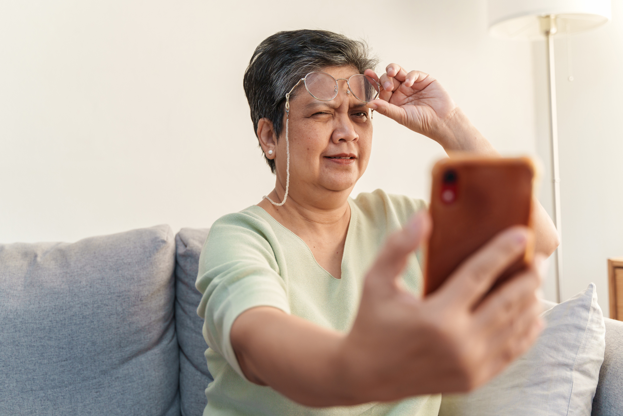 A woman squints at a phone screen, appearing confused or struggling to see