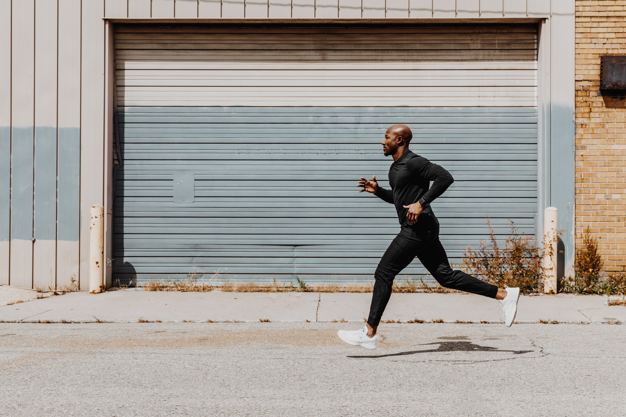A man in athletic wear jogging on a sidewalk by a building with garage doors
