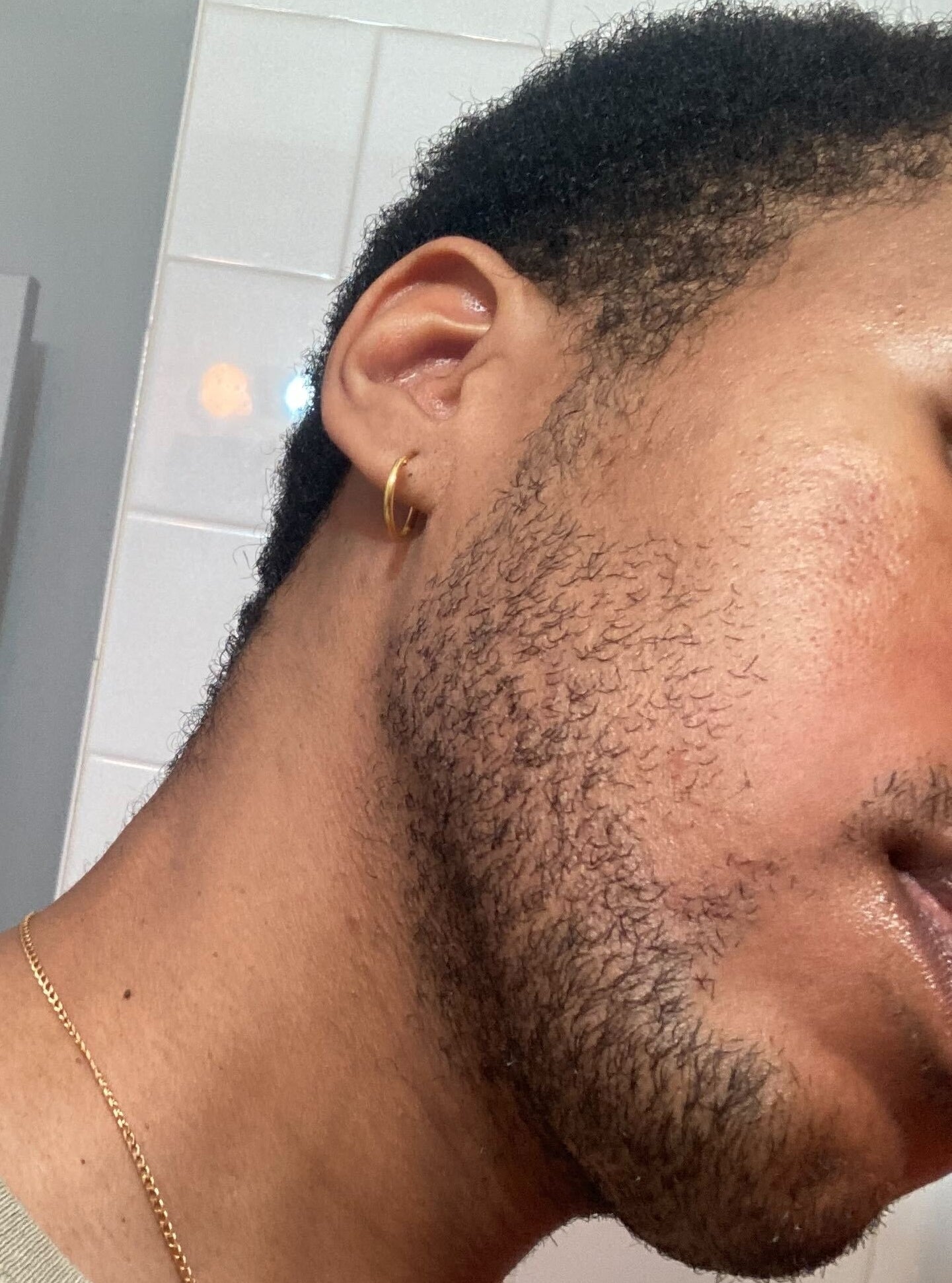 Close-up of a person's jawline and neck, with partial view of an ear with an earring, wearing a sweater