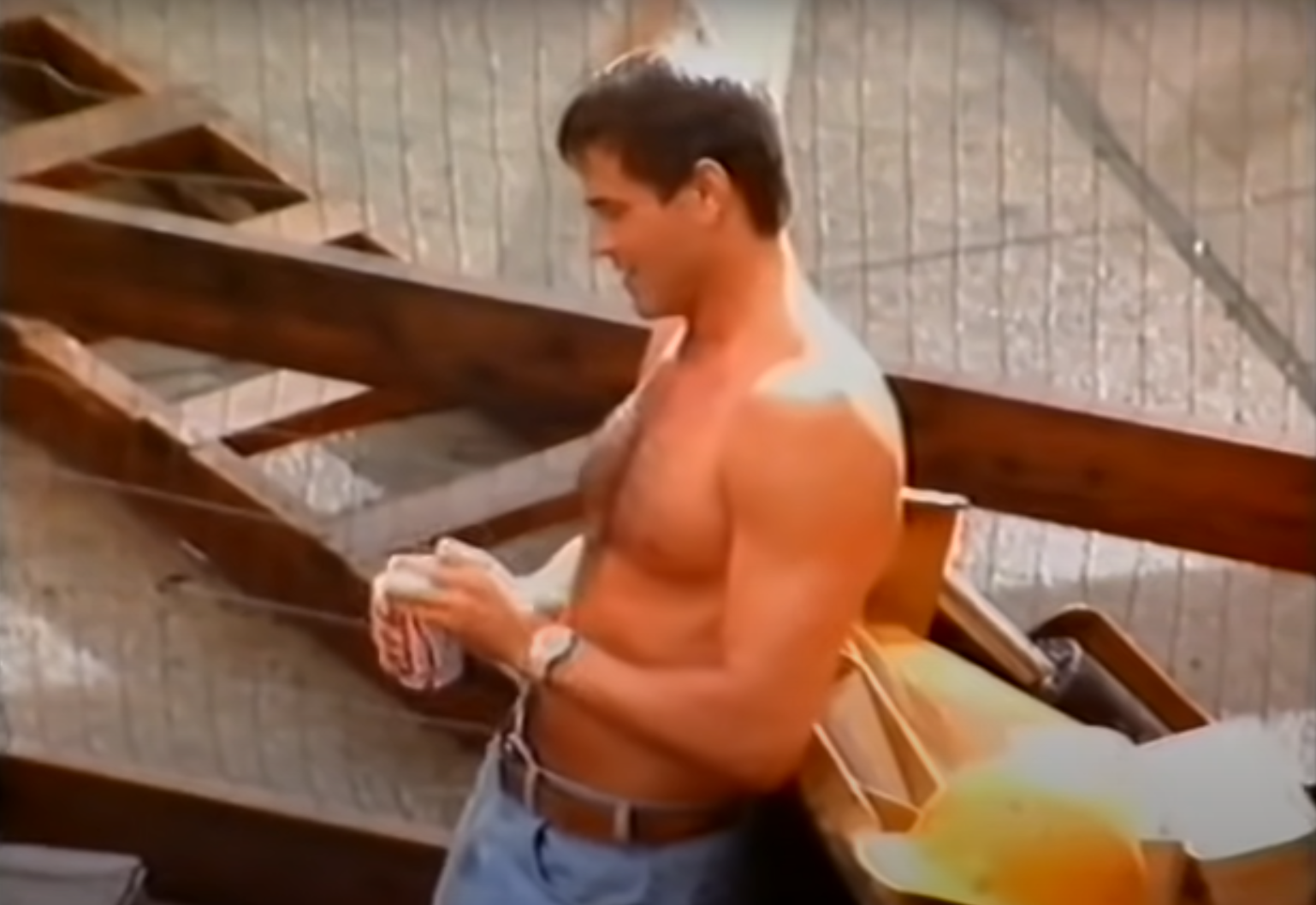 Man in jeans with a construction backdrop, holding a tool, reminiscent of a scene from a past era