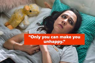 Woman lying in bed with a concerned expression, surrounded by plush toys, looking at a smartphone