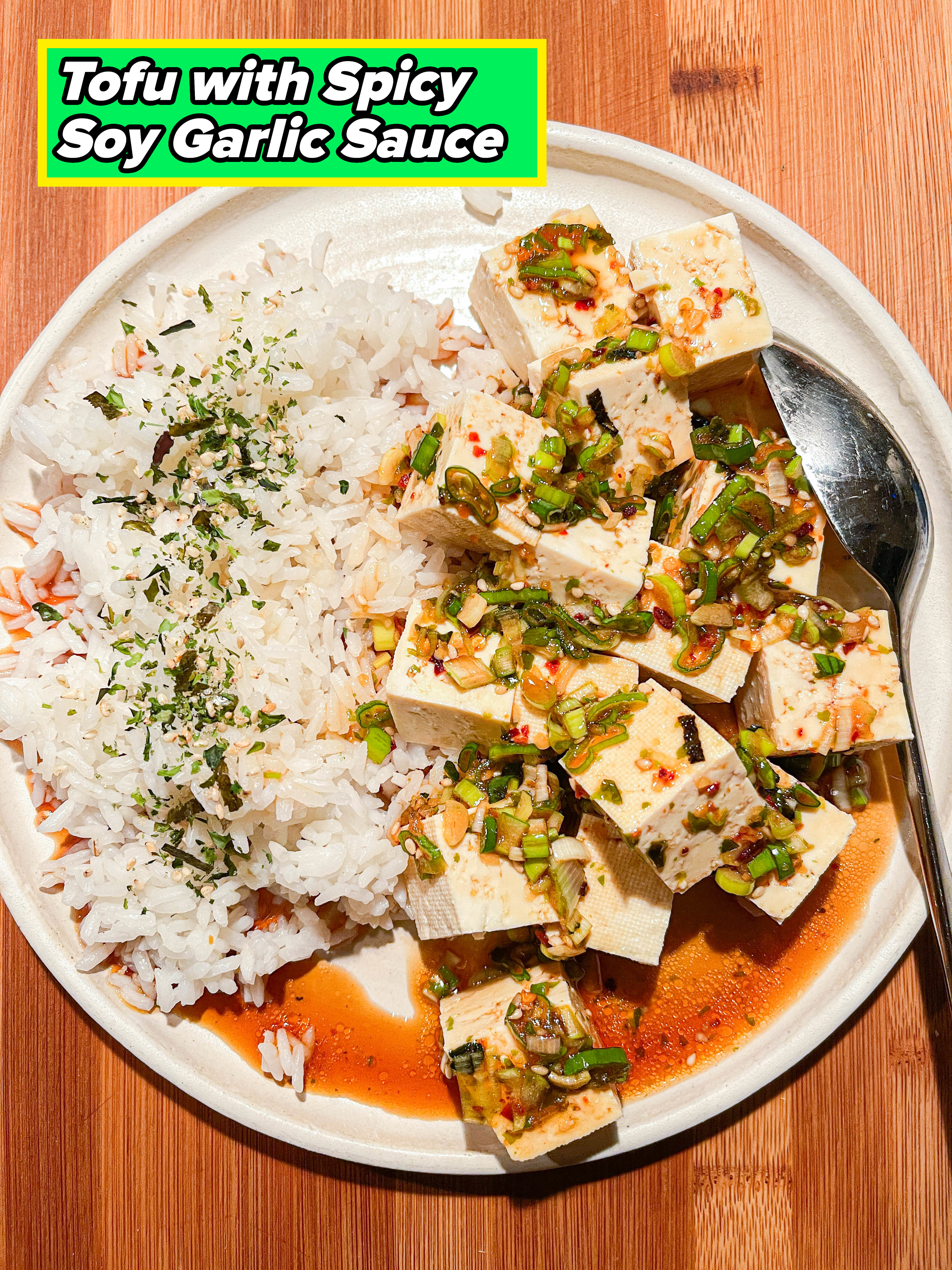 Plate of rice with tofu topped with green onions and sauce on a wooden table