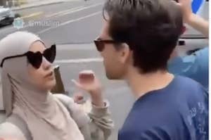 ヒジャブを着用した女性と青シャツの男性が歩道で対話している。