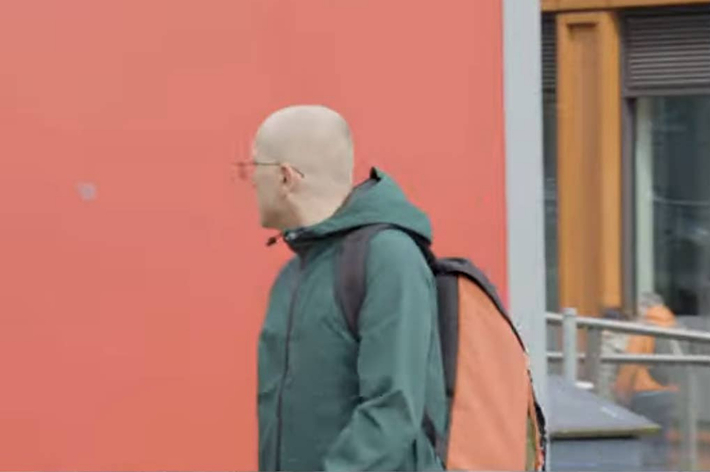 男性がリュックを背負い街を歩いている。