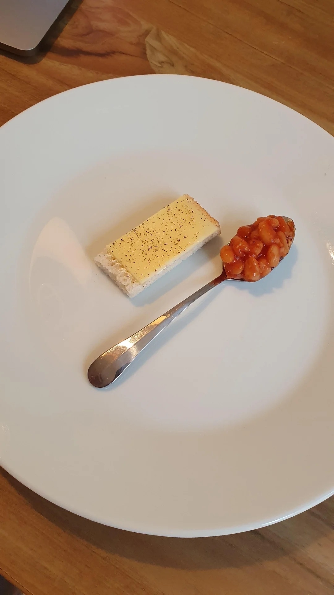 A plate with a cracker topped with cheese beside a spoonful of baked beans