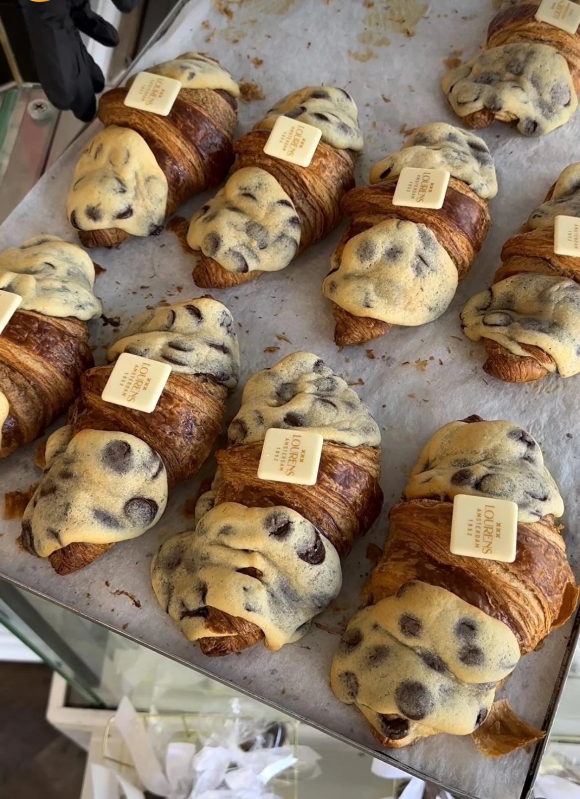 Assorted croissants with toppings on a tray in a bakery display. Some have a chocolate chip topping