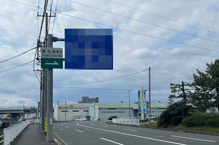 電柱と案内看板がある道路沿いの景色です。看板には大きなテキストが含まれています。