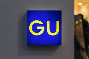 Signboard with the logo of GU, a clothing brand, on a wall
