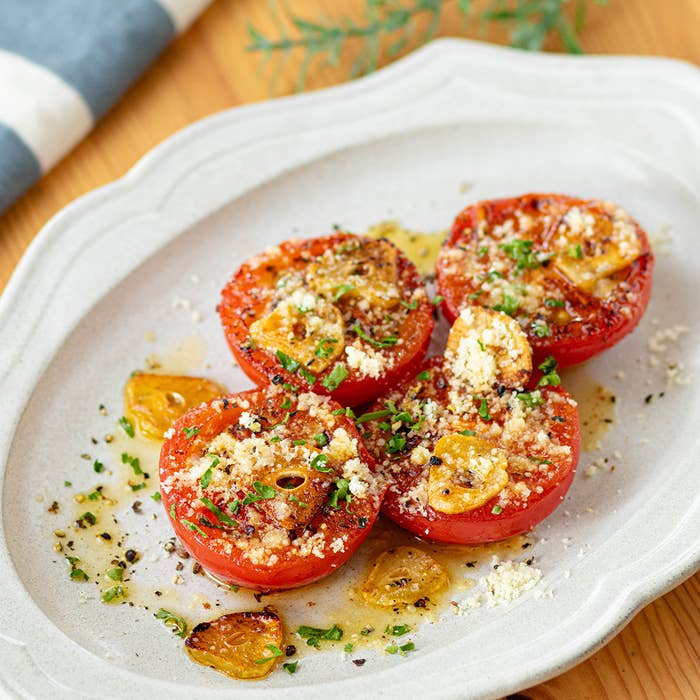 皿の上のハーブとチーズをふりかけたオーブン焼きトマト。