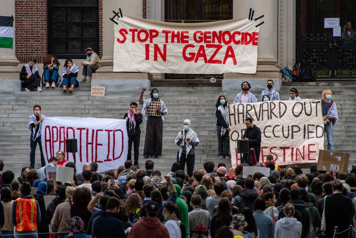 Protesters with banners advocating against conflict in Gaza and banner saying &quot;STOP THE GENOCIDE IN GAZA&quot; in background