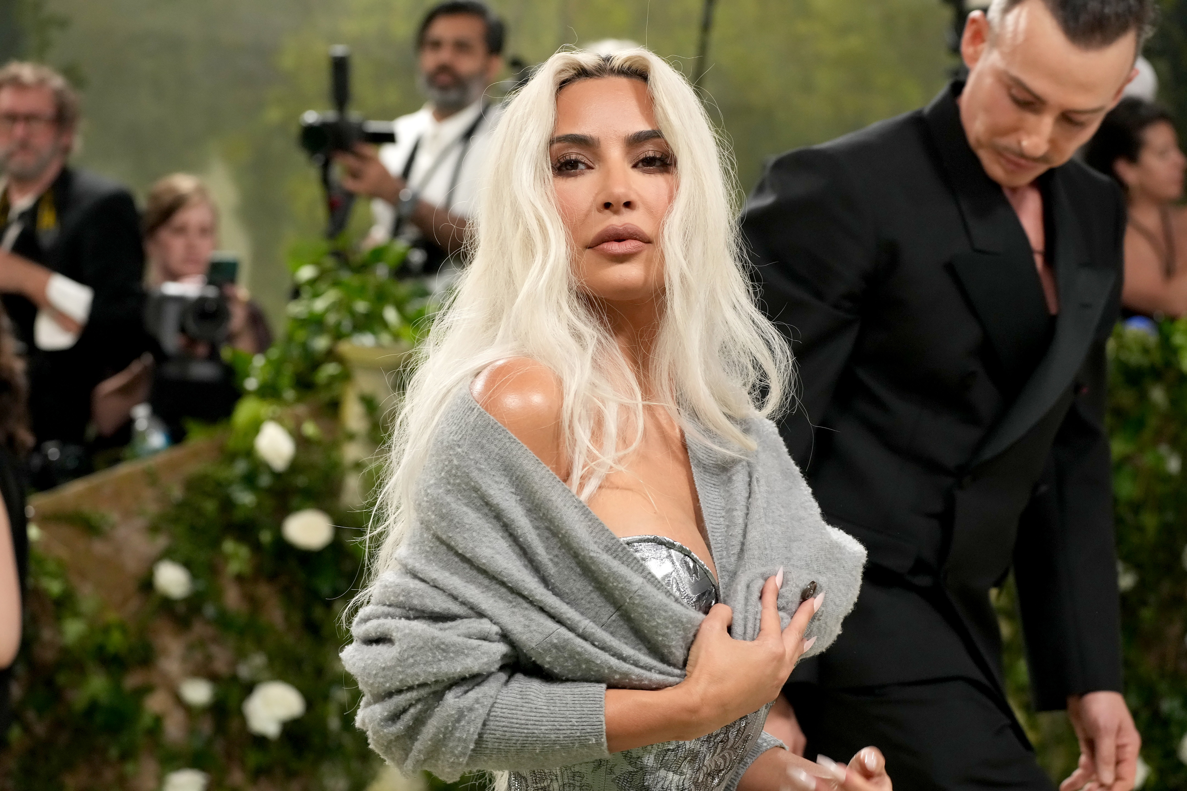 Kim Kardashian in a metallic dress with draped shawl on her arms at an event