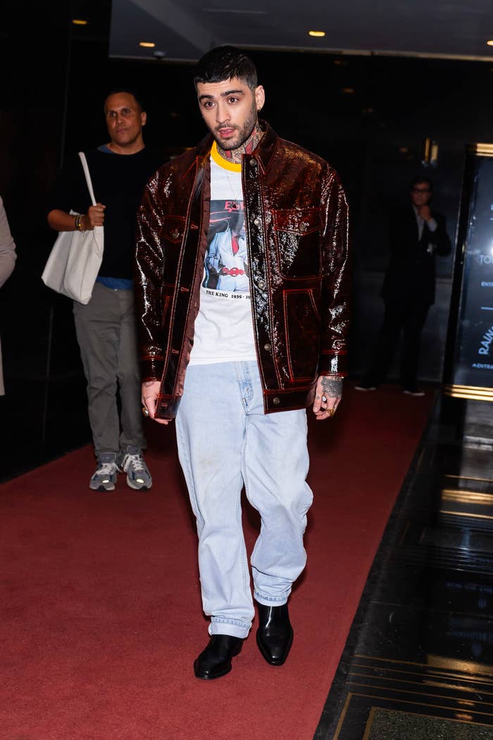 Zayn Malik walking on red carpet in a sequined jacket, graphic t-shirt, and loose-fitting jeans